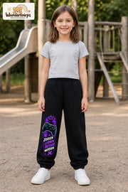 Mädchen trägt schwarze Jogginghose mit Gaming Sterne Violett-Print, von vorn auf dem Spielplatz.