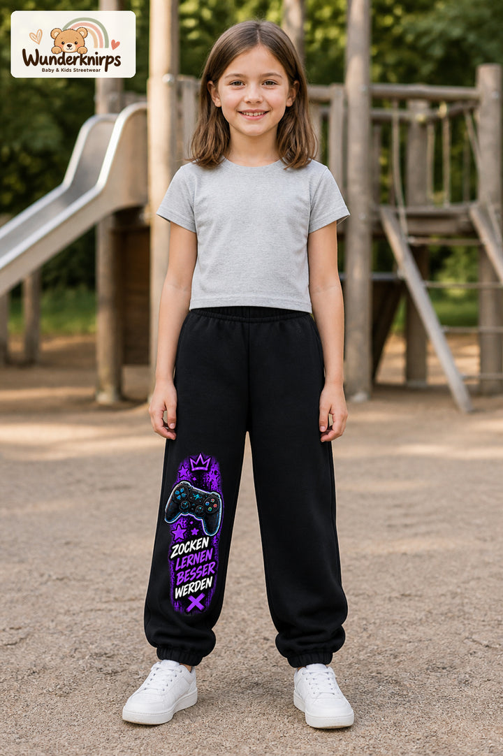 Mädchen trägt schwarze Jogginghose mit Gaming Sterne Violett-Print, von vorn auf dem Spielplatz.