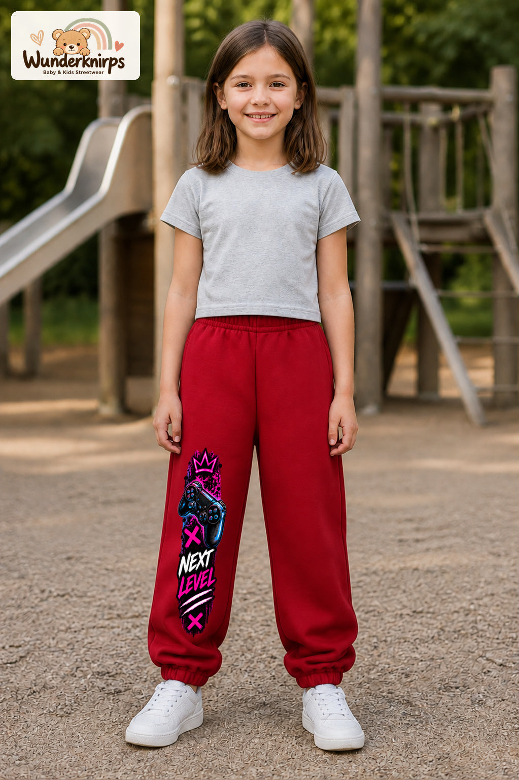 Mädchen trägt rote Jogginghose mit Next Level Controller-Print, von vorn auf dem Spielplatz.
