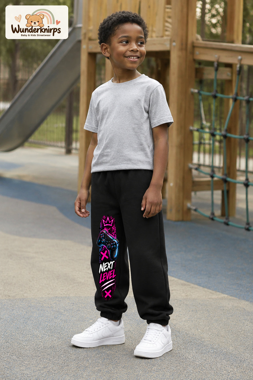 Junge trägt schwarze Jogginghose mit Next Level Controller-Print, leicht seitlich auf dem Spielplatz.