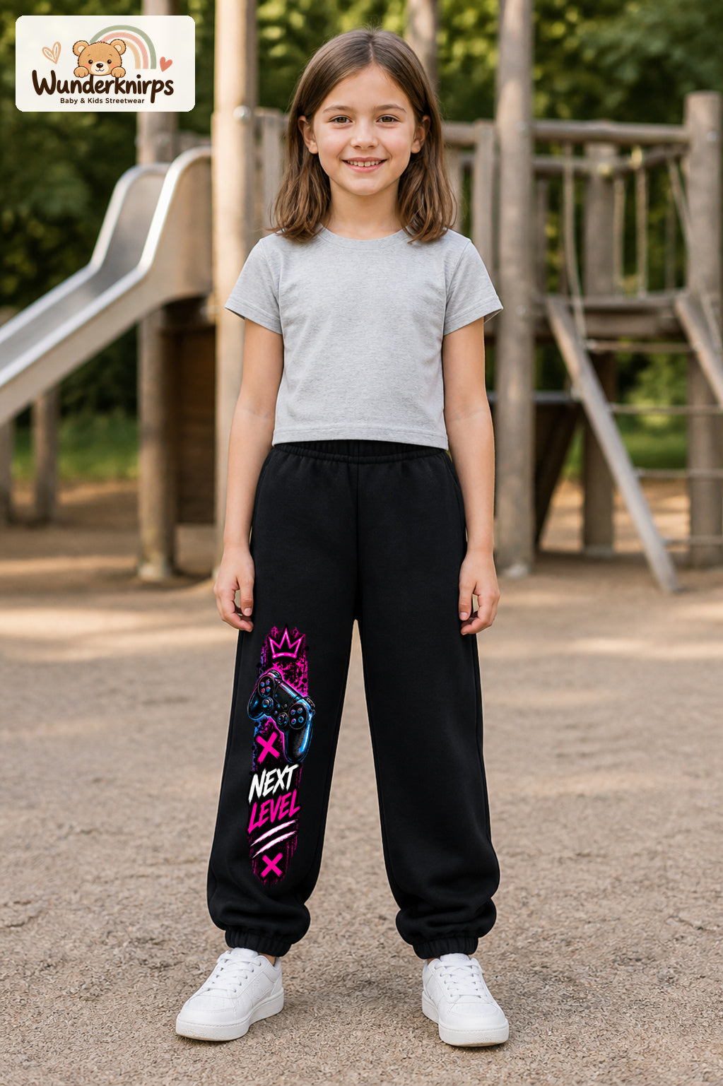 Mädchen trägt schwarze Jogginghose mit Next Level Controller-Print, von vorn auf dem Spielplatz.