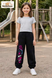 Mädchen trägt schwarze Jogginghose mit Next Level Controller-Print, von vorn auf dem Spielplatz.