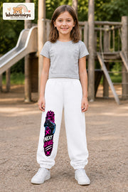 Mädchen trägt weiße Jogginghose mit Next Level Controller-Print, von vorn auf dem Spielplatz.
