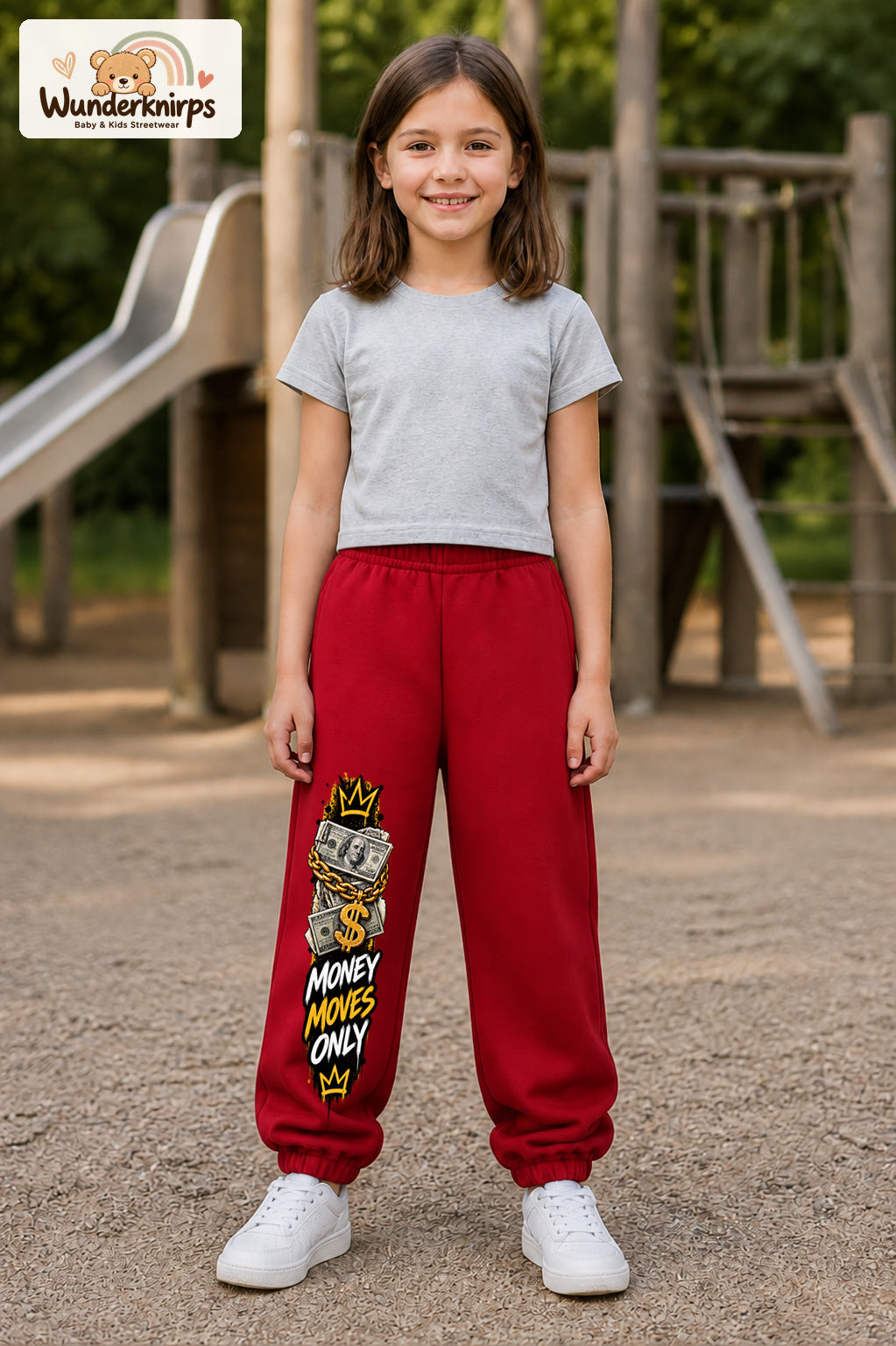 Mädchen trägt rote Jogginghose mit Money Moves Gold-Print, von vorn auf dem Spielplatz.