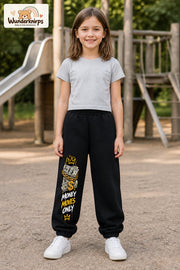 Mädchen trägt schwarze Jogginghose mit Money Moves Gold-Print, von vorn auf dem Spielplatz.