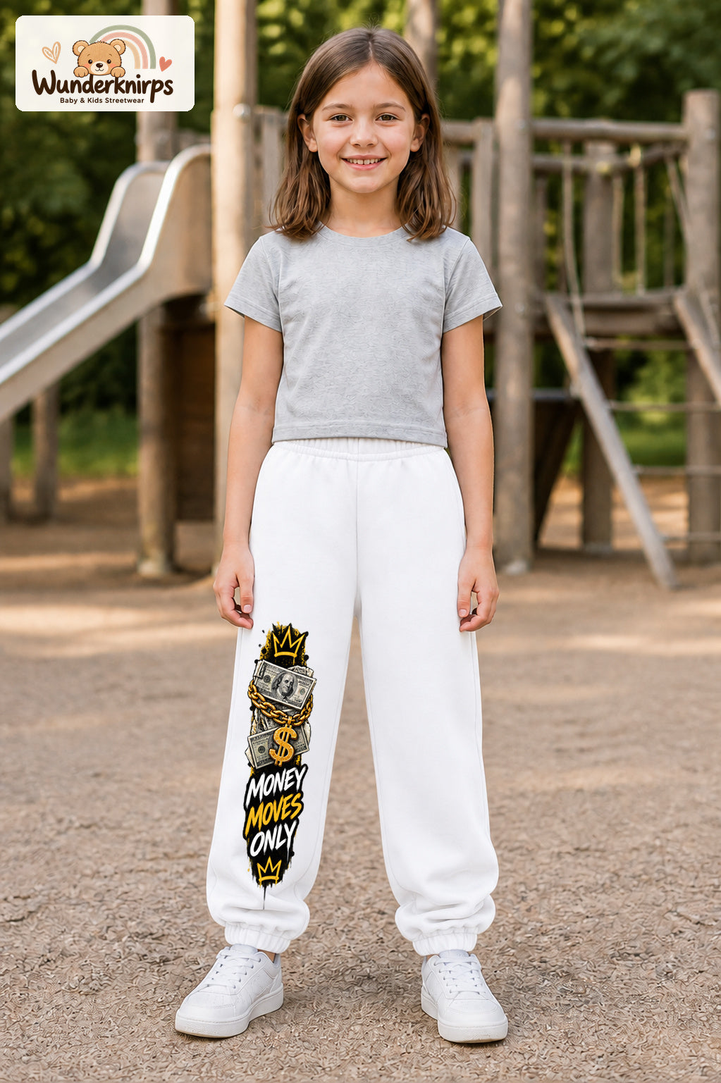 Mädchen trägt weiße Jogginghose mit Money Moves Gold-Print, von vorn auf dem Spielplatz.
