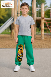 Junge trägt grüne Jogginghose mit Neugierig Giraffe-Print, von vorn auf dem Spielplatz.