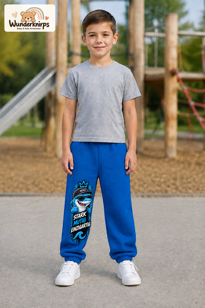 Junge trägt blaue Jogginghose mit Stark einzigartig Cap-Hai-Print, von vorn auf dem Spielplatz.