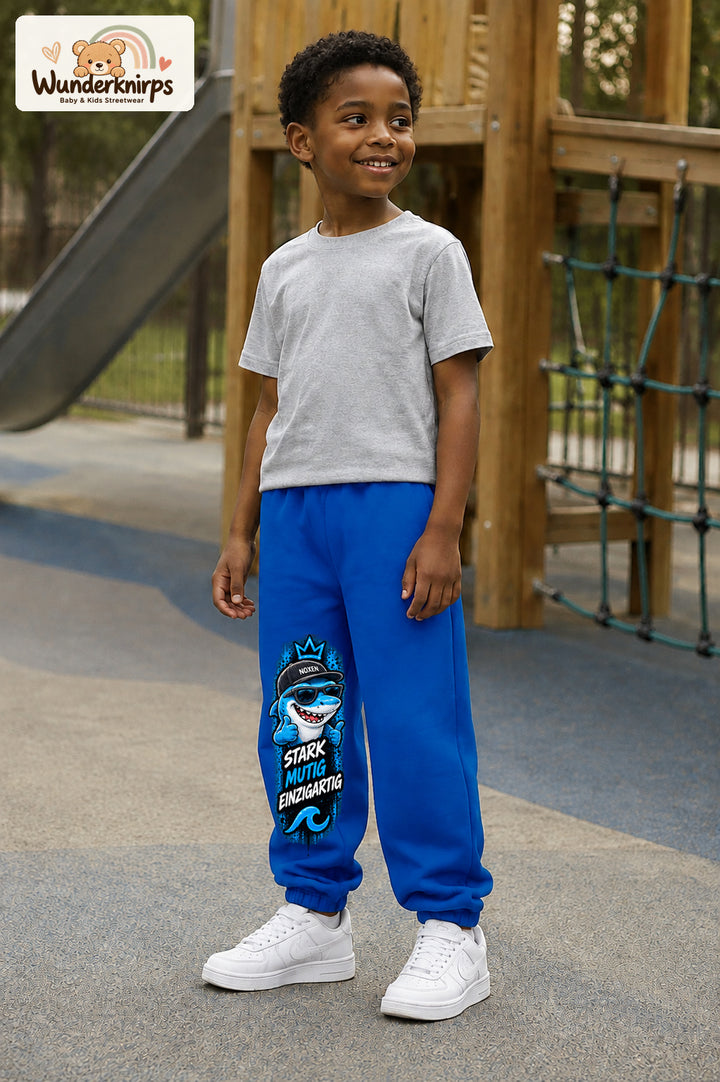 Junge trägt blaue Jogginghose mit Stark einzigartig Cap-Hai-Print, leicht seitlich auf dem Spielplatz.
