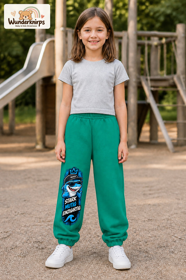 Mädchen trägt grüne Jogginghose mit Stark einzigartig Cap-Hai-Print, von vorn auf dem Spielplatz.