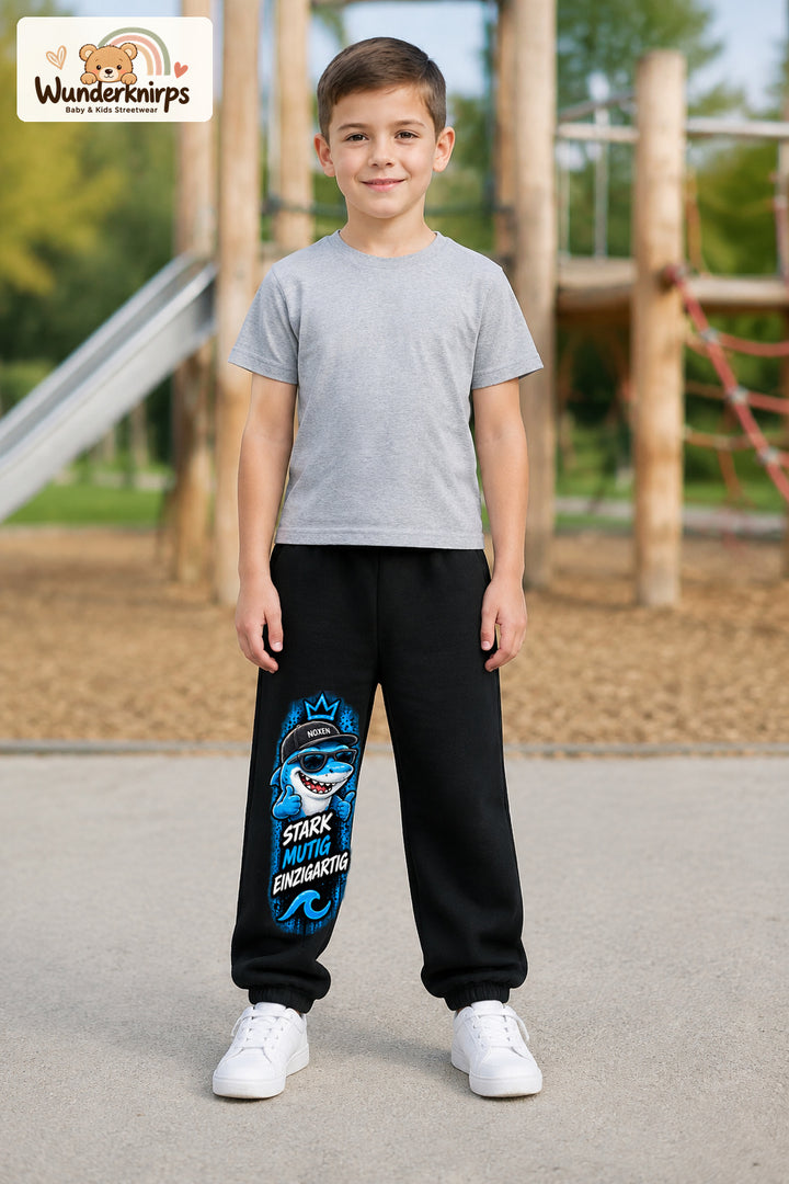 Junge trägt schwarze Jogginghose mit Stark einzigartig Cap-Hai-Print, von vorn auf dem Spielplatz.