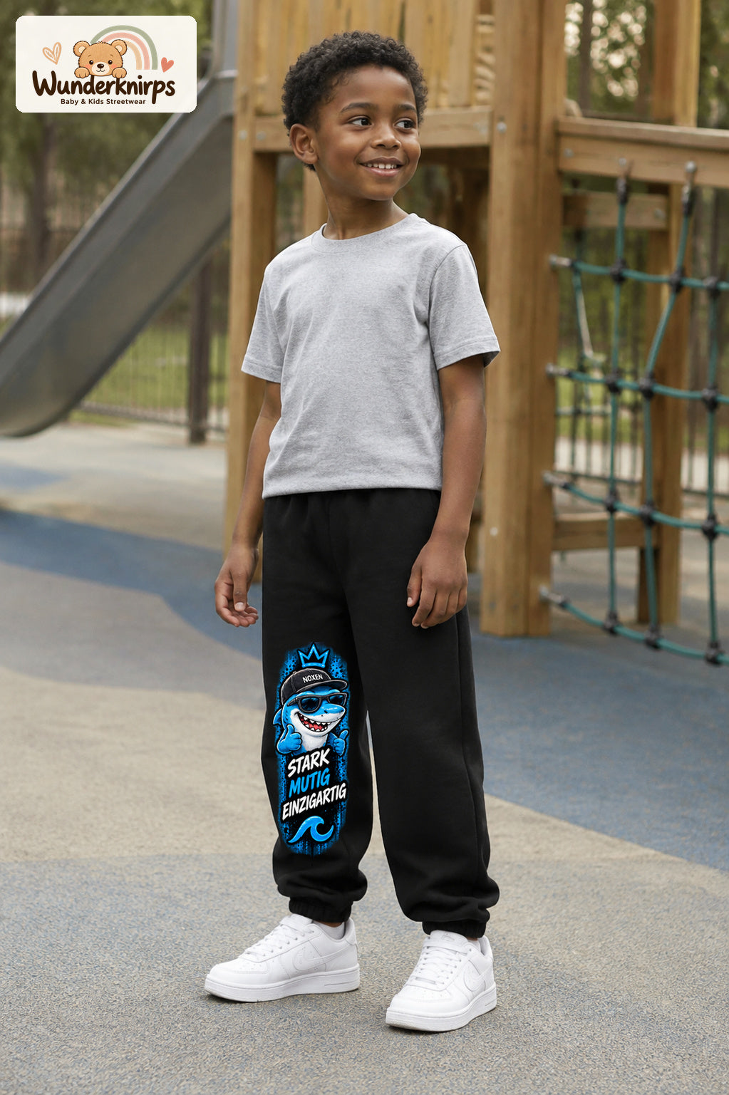 Junge trägt schwarze Jogginghose mit Stark einzigartig Cap-Hai-Print, leicht seitlich auf dem Spielplatz.