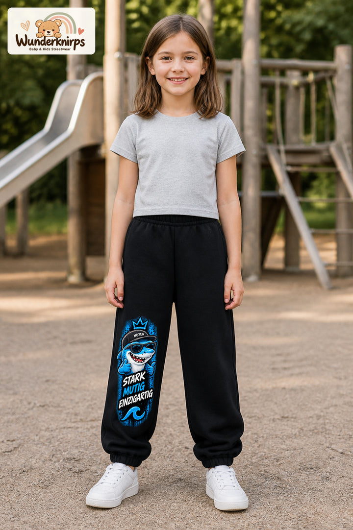 Mädchen trägt schwarze Jogginghose mit Stark einzigartig Cap-Hai-Print, von vorn auf dem Spielplatz.