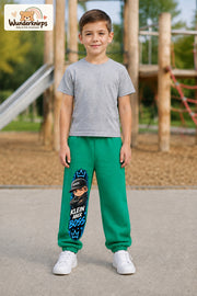Junge trägt grüne Jogginghose mit Klein aber Boss Cap-Print, von vorn auf dem Spielplatz.