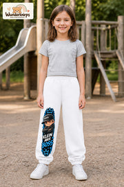 Mädchen trägt weiße Jogginghose mit Klein aber Boss Cap-Print, von vorn auf dem Spielplatz.
