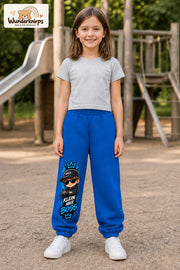 Mädchen trägt blaue Jogginghose mit Klein aber Boss Sonnenbrille-Print, von vorn auf dem Spielplatz.