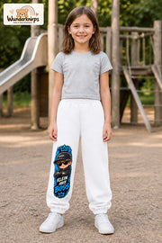 Mädchen trägt weiße Jogginghose mit Klein aber Boss Sonnenbrille-Print, von vorn auf dem Spielplatz.