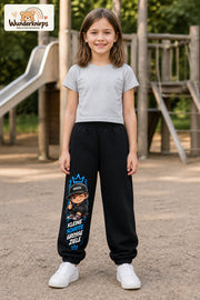 Mädchen trägt schwarze Jogginghose mit Kleine Schritte Skater-Print, von vorn auf dem Spielplatz.