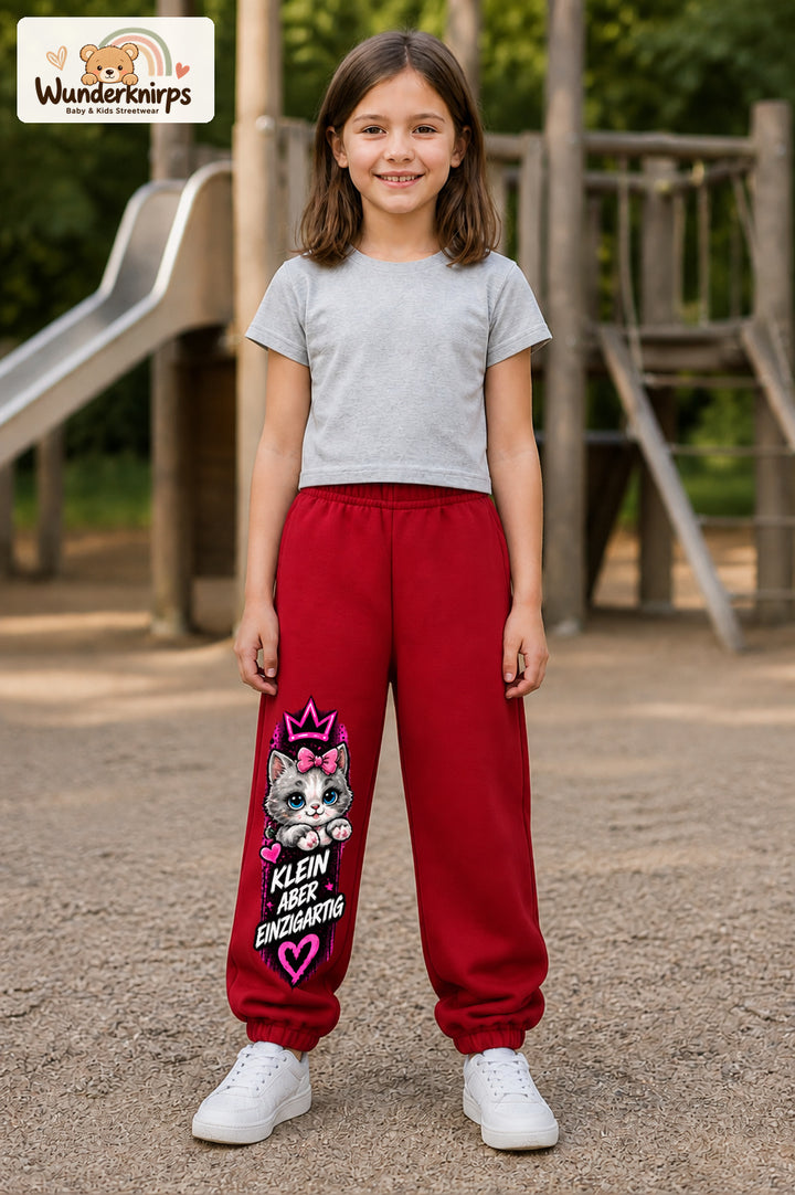 Mädchen trägt rote Jogginghose mit Klein einzigartig Katze-Print, von vorn auf dem Spielplatz.
