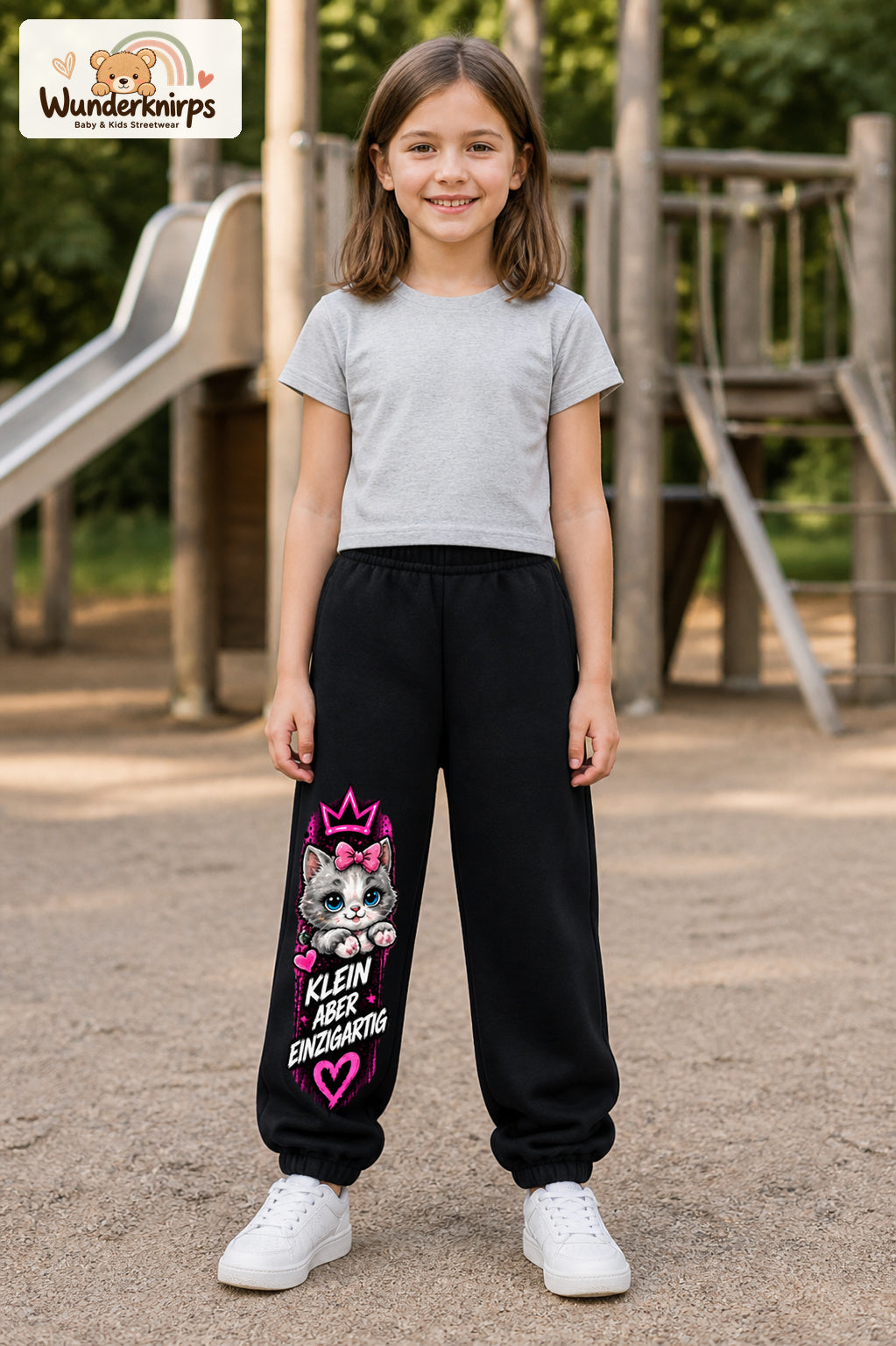 Mädchen trägt schwarze Jogginghose mit Klein einzigartig Katze-Print, von vorn auf dem Spielplatz.