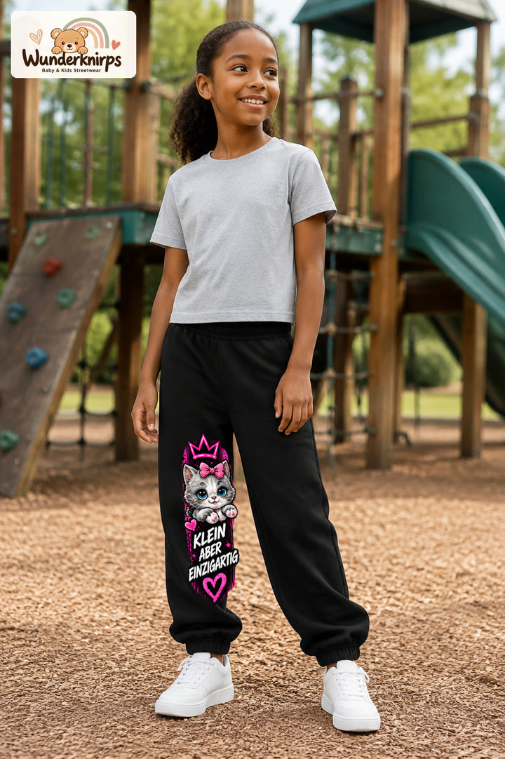Mädchen trägt schwarze Jogginghose mit Klein einzigartig Katze-Print, leicht seitlich auf dem Spielplatz.