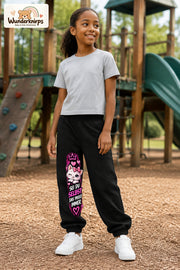 Mädchen trägt schwarze Jogginghose mit Sei du selbst Kätzchen-Print, leicht seitlich auf dem Spielplatz.