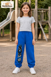 Mädchen trägt blaue Jogginghose mit Große Träume Mini-Boss-Print, von vorn auf dem Spielplatz.