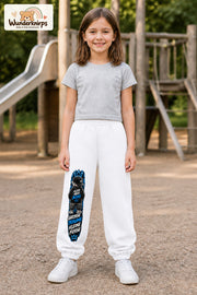 Mädchen trägt weiße Jogginghose mit Große Träume Mini-Boss-Print, von vorn auf dem Spielplatz.
