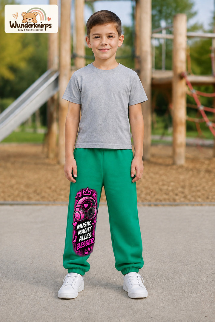 Junge trägt grüne Jogginghose mit Musik macht besser-Print, von vorn auf dem Spielplatz.