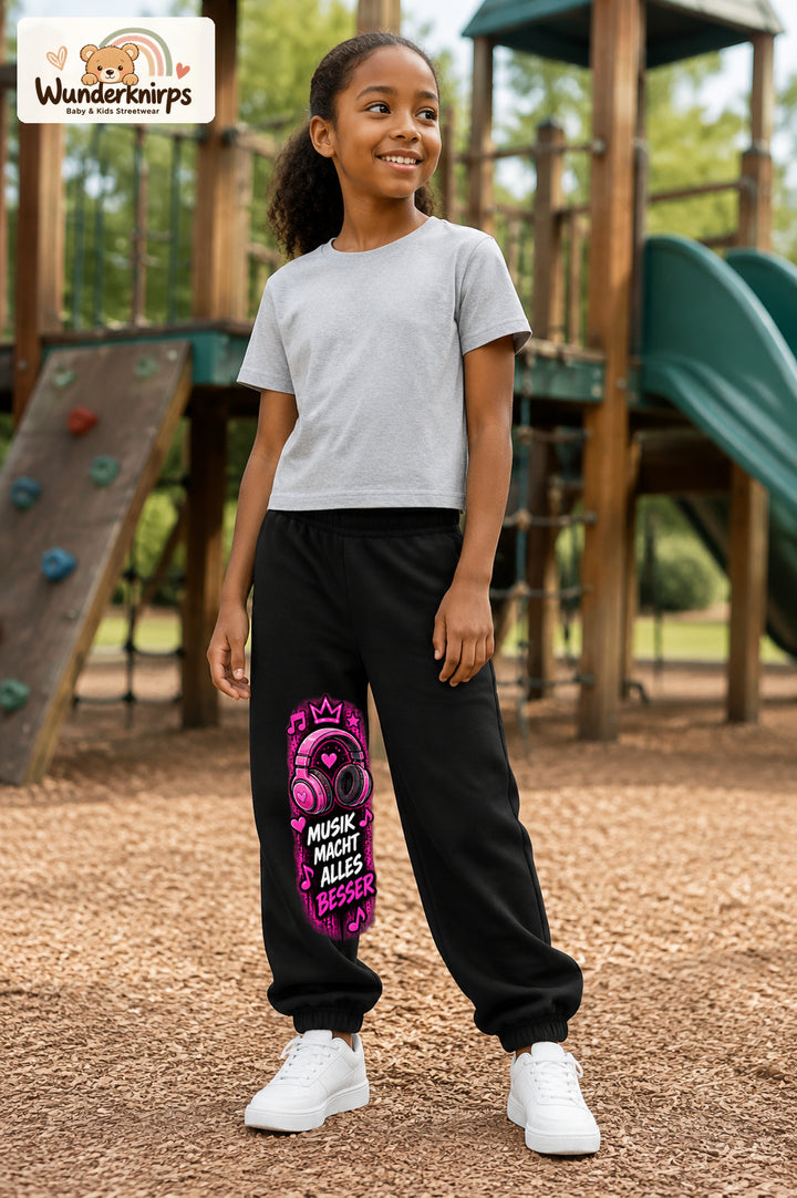 Mädchen trägt schwarze Jogginghose mit Musik macht besser-Print, leicht seitlich auf dem Spielplatz.