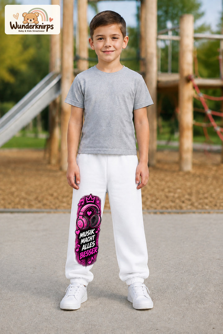 Junge trägt weiße Jogginghose mit Musik macht besser-Print, von vorn auf dem Spielplatz.
