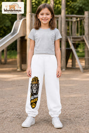 Mädchen trägt weiße Jogginghose mit Alpha Mode Löwe-Print, von vorn auf dem Spielplatz.