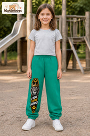 Mädchen trägt grüne Jogginghose mit Lebe deine Stärke Löwe-Print, von vorn auf dem Spielplatz.