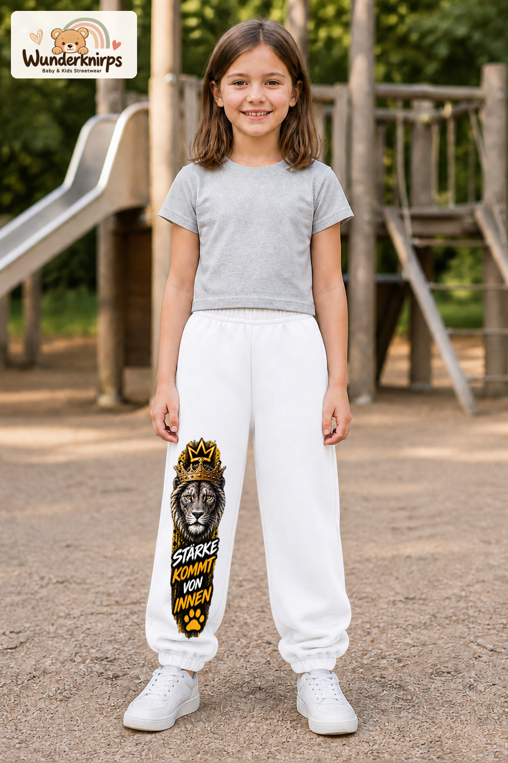 Mädchen trägt weiße Jogginghose mit Stärke von innen Löwe-Print, von vorn auf dem Spielplatz.