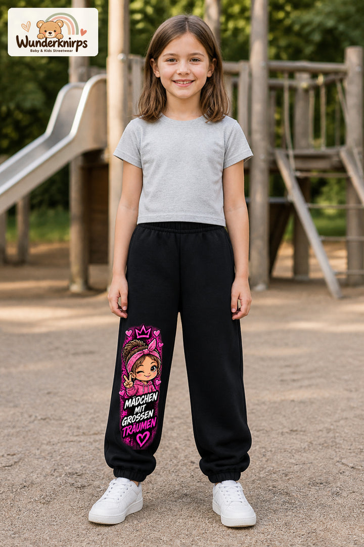 Mädchen trägt schwarze Jogginghose mit Große Träume Herz-Bandana-Print, von vorn auf dem Spielplatz.