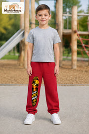 Junge trägt rote Jogginghose mit Higher Life Palmen-Print, von vorn auf dem Spielplatz.