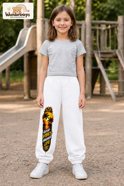 Mädchen trägt weiße Jogginghose mit Higher Life Palmen-Print, von vorn auf dem Spielplatz.