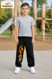 Junge trägt schwarze Jogginghose mit Good Vibes Sonnenuntergang-Print, von vorn auf dem Spielplatz.