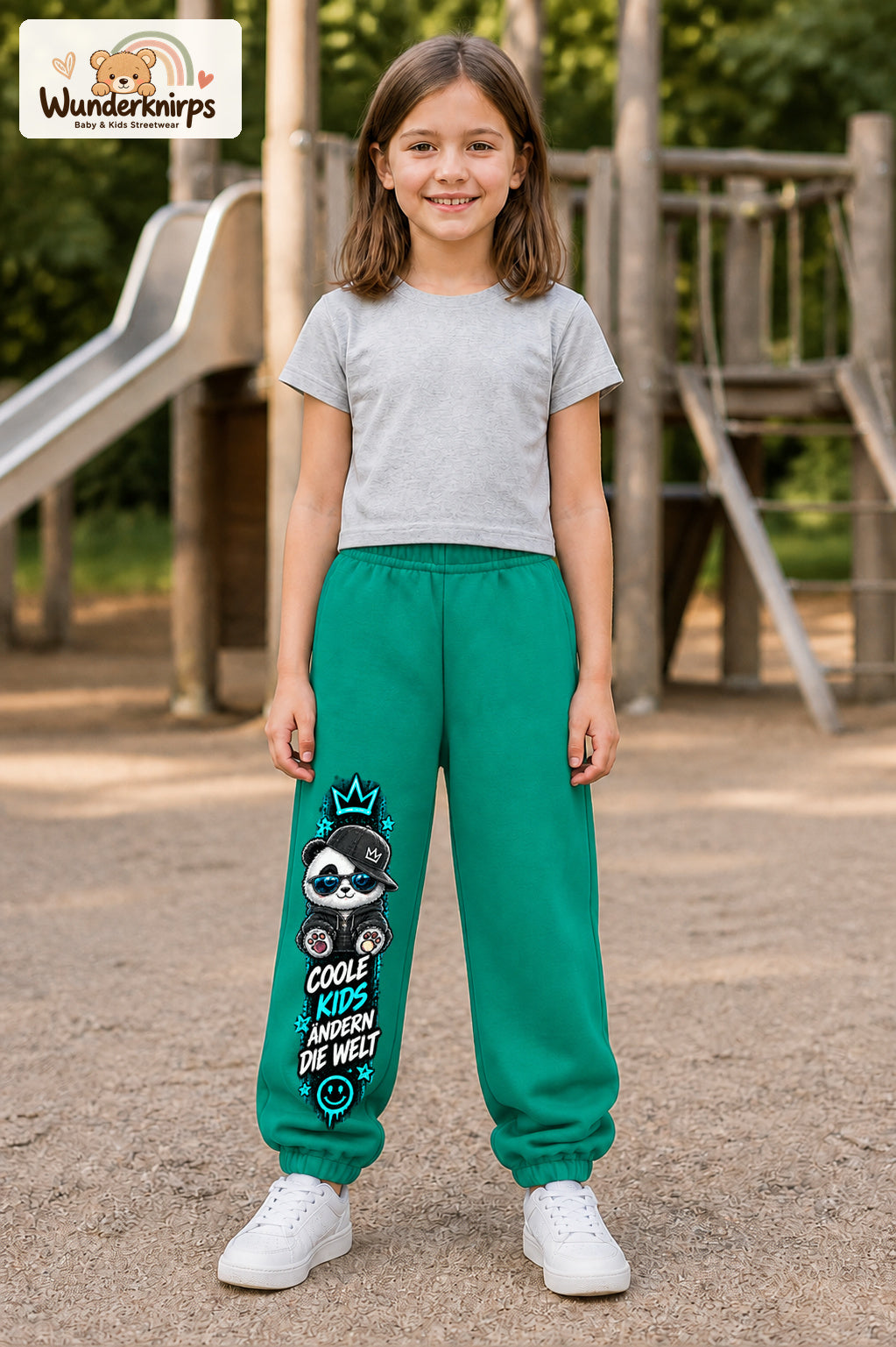 Mädchen trägt grüne Jogginghose mit Coole Kids Panda-Print, von vorn auf dem Spielplatz.