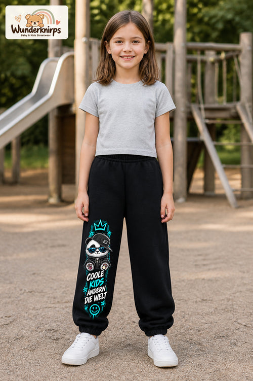 Mädchen trägt schwarze Jogginghose mit Coole Kids Panda-Print, von vorn auf dem Spielplatz.