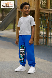 Junge trägt blaue Jogginghose mit Sei du selbst Panda-Print, leicht seitlich auf dem Spielplatz.