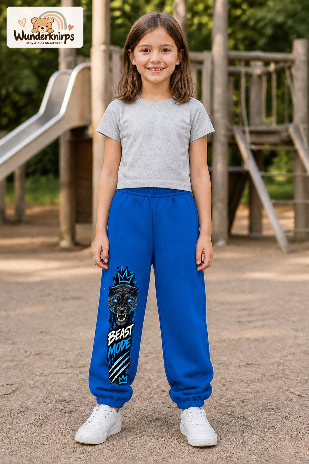Mädchen trägt blaue Jogginghose mit Beast Mode Panther-Print, von vorn auf dem Spielplatz.