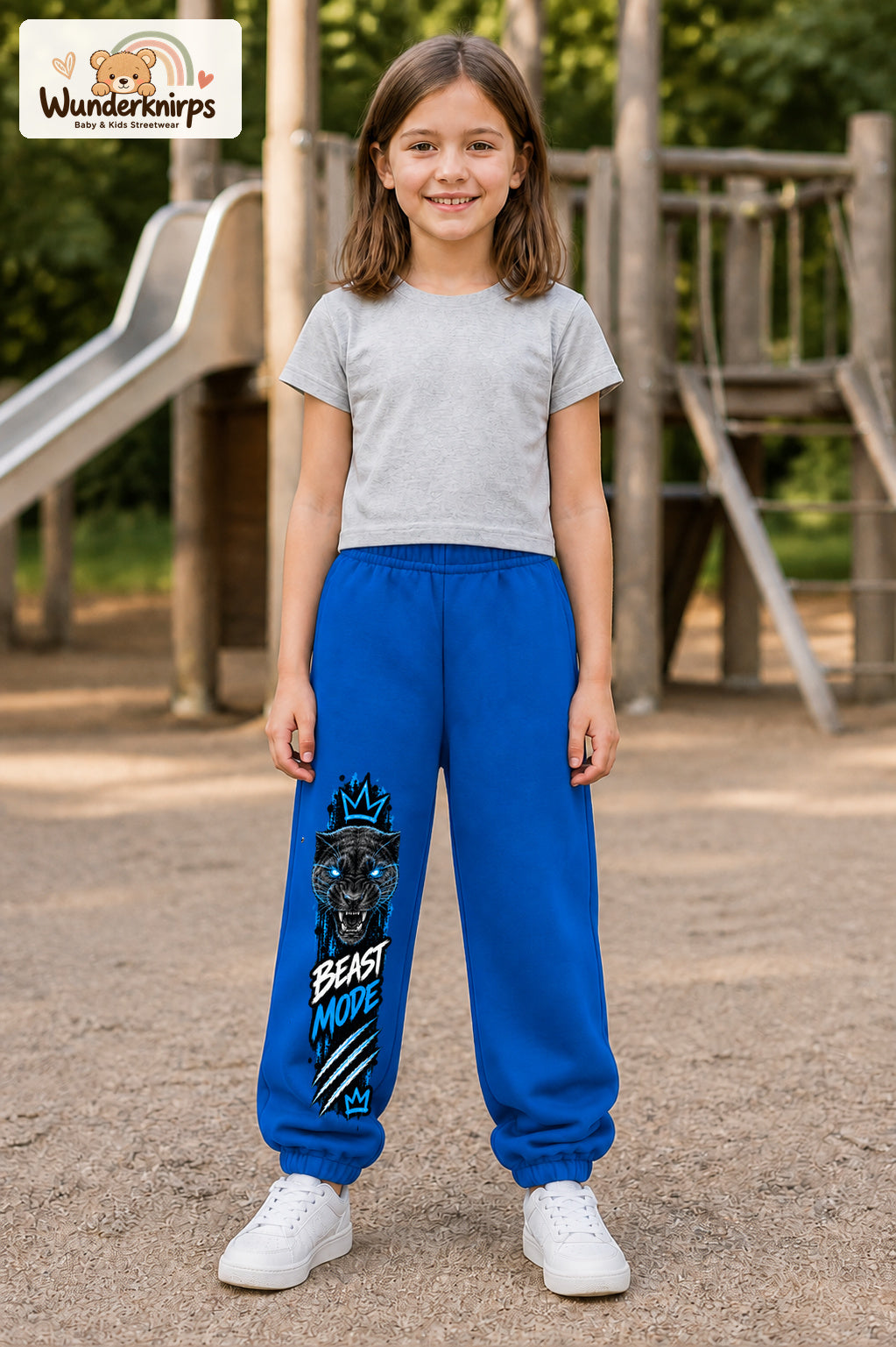 Mädchen trägt blaue Jogginghose mit Beast Mode Panther-Print, von vorn auf dem Spielplatz.
