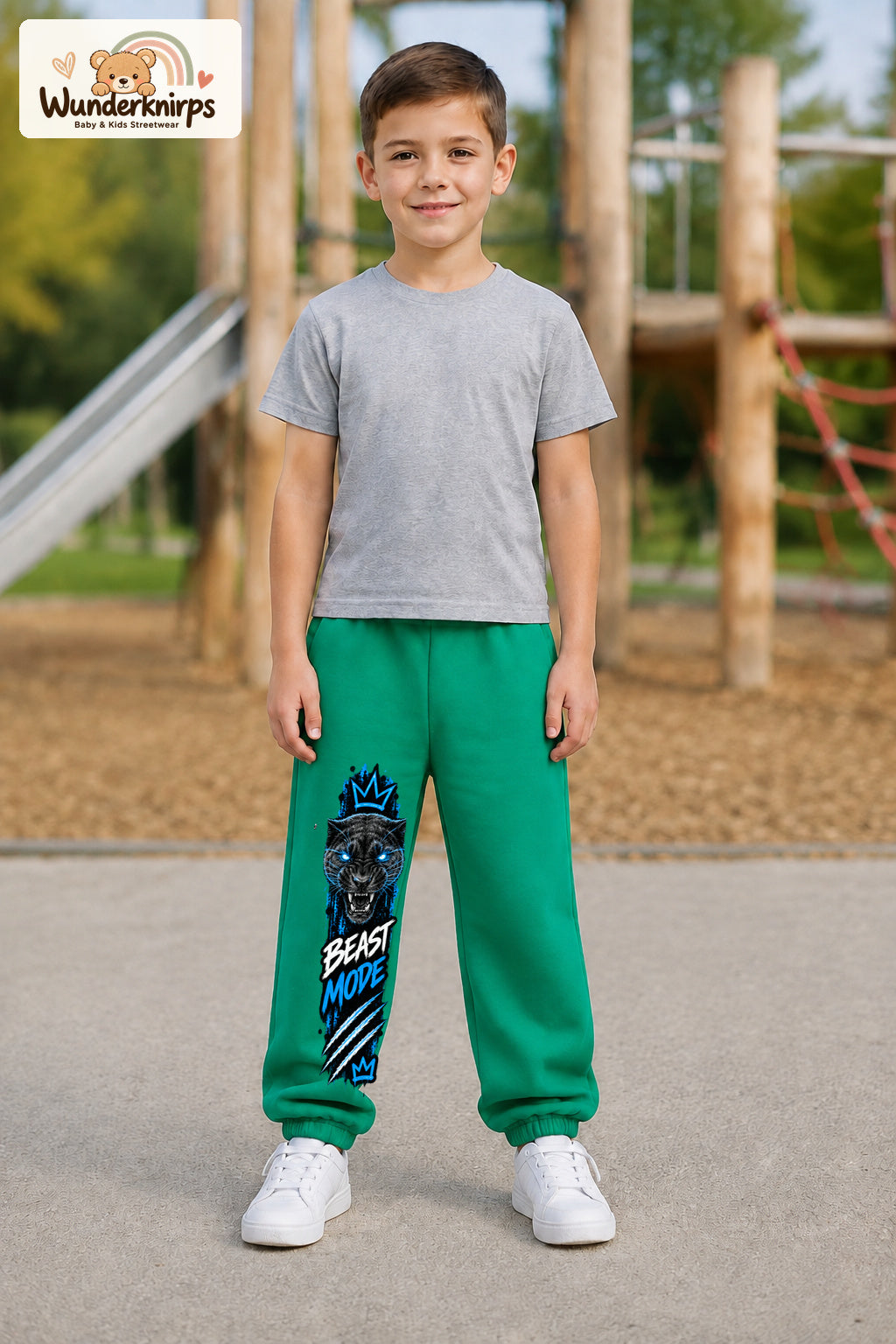 Junge trägt grüne Jogginghose mit Beast Mode Panther-Print, von vorn auf dem Spielplatz.
