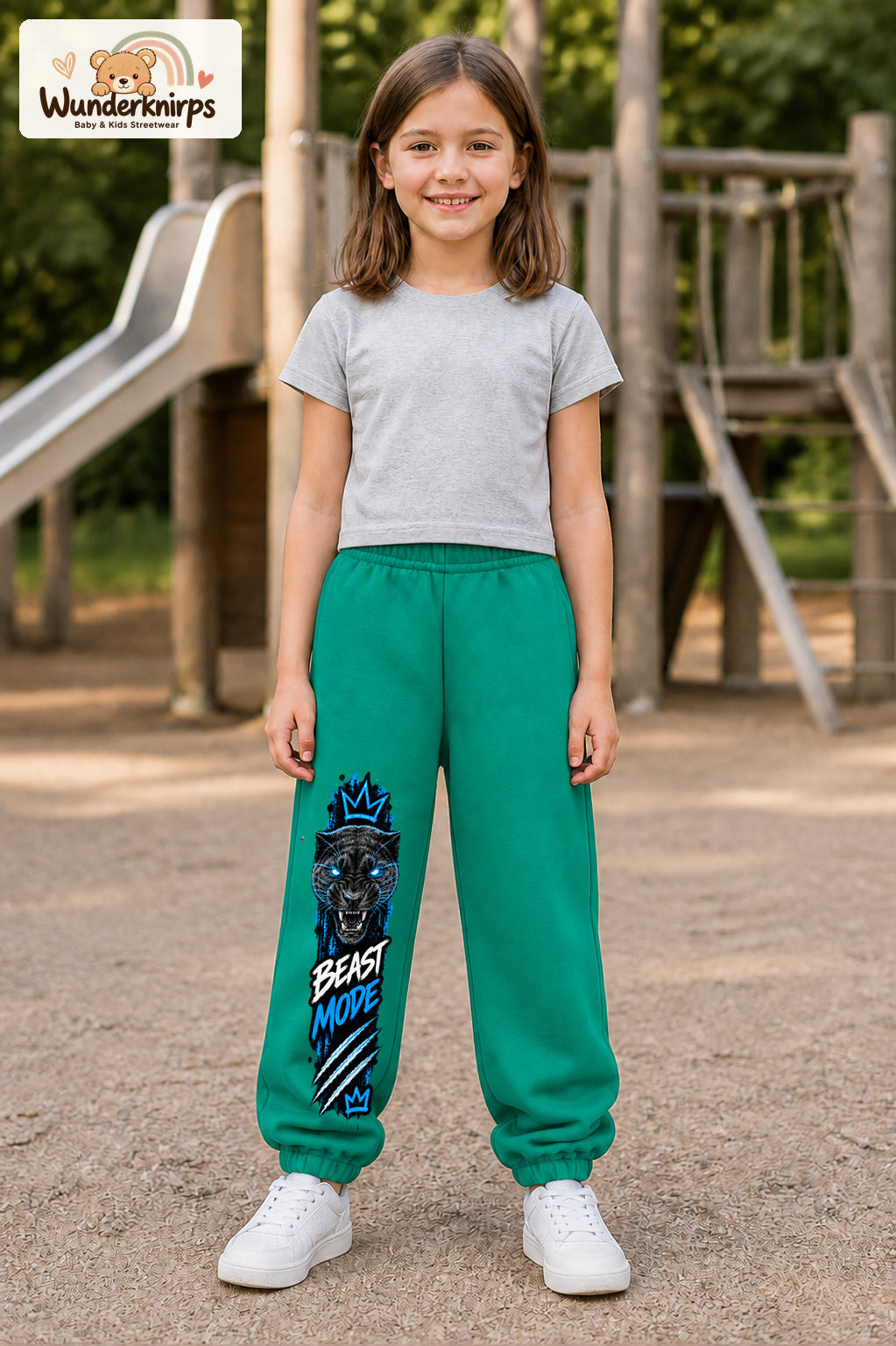 Mädchen trägt grüne Jogginghose mit Beast Mode Panther-Print, von vorn auf dem Spielplatz.
