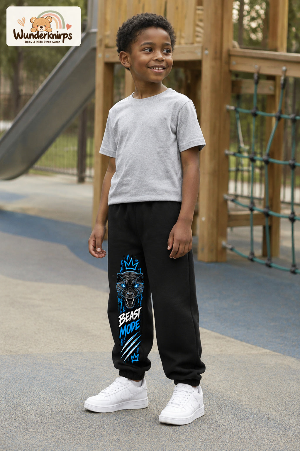Junge trägt schwarze Jogginghose mit Beast Mode Panther-Print, leicht seitlich auf dem Spielplatz.