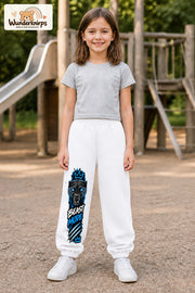 Mädchen trägt weiße Jogginghose mit Beast Mode Panther-Print, von vorn auf dem Spielplatz.