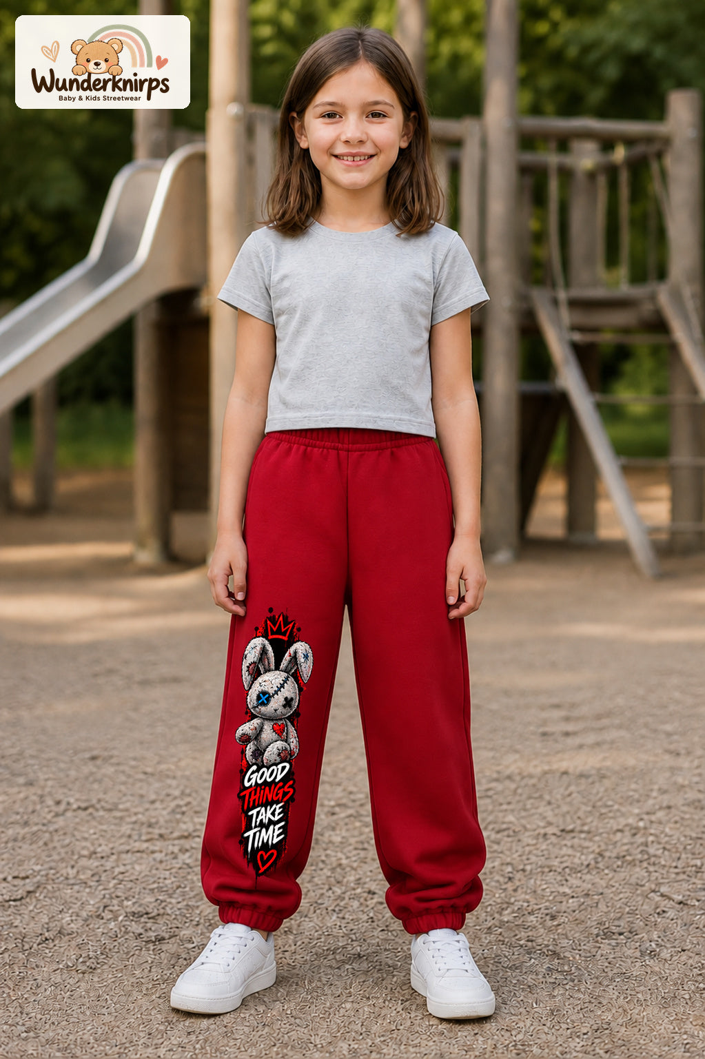 Mädchen trägt rote Jogginghose mit Good Things Stoffhase-Print, von vorn auf dem Spielplatz.