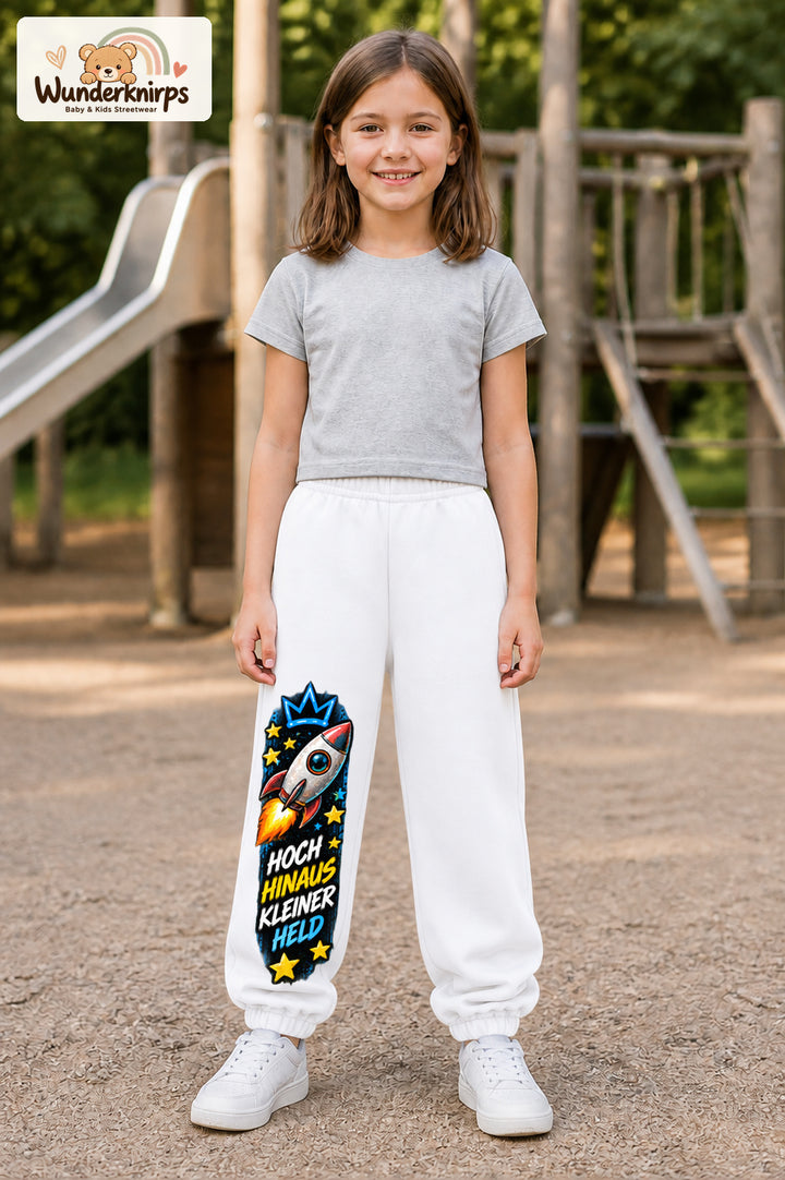 Mädchen trägt weiße Jogginghose mit Hoch hinaus Rakete-Print, von vorn auf dem Spielplatz.