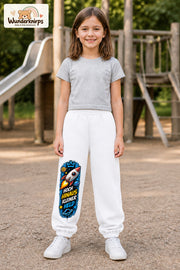 Mädchen trägt weiße Jogginghose mit Kleiner Held Weltraumrakete-Print, von vorn auf dem Spielplatz.